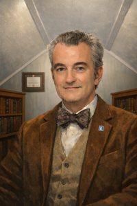 Portrait of Doug Berry, Abilene, Texas REALTOR®, wearing a bow tie and jacket, standing in a study with bookshelves in the background.